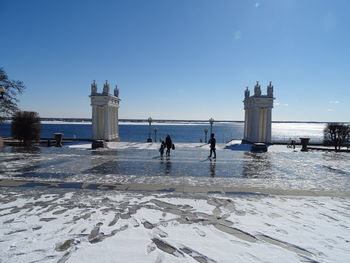 People on snow covered land by sea against sky