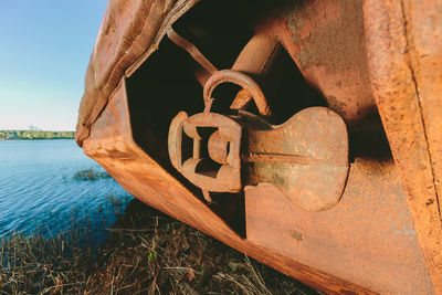 Close-up of rusty metallic structure by lake against sky