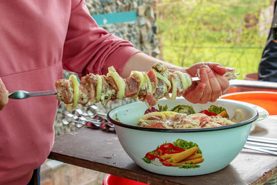 A bowl filled with marinated raw meat and women's hands stringing kebabs on a skewer