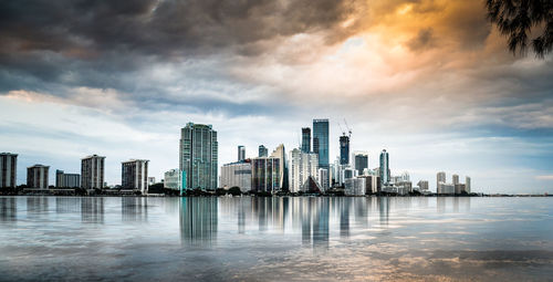 View of city at waterfront against cloudy sky