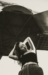 Low angle view of young woman standing against sky