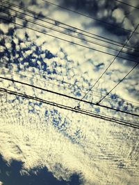 Low angle view of electricity pylon against cloudy sky