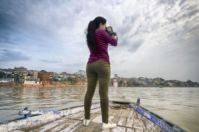Rear view of woman photographing while standing on boat in river