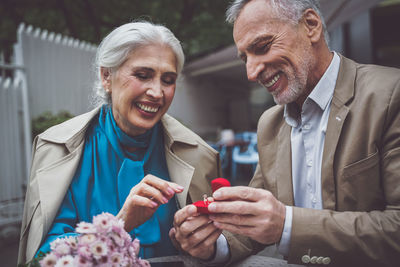 Smiling senior man giving ring to wife while sitting at cafe