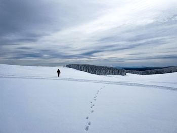 Footsteps in the snow left by a hiker seen in the distance on a cloudy day in the mountains