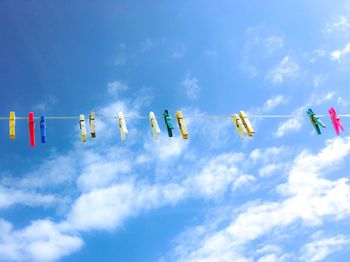 Low angle view of colorful clothespins hanging on clothesline against sky during sunny day
