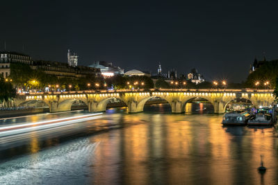 Illuminated bridge over river against sky in city at night