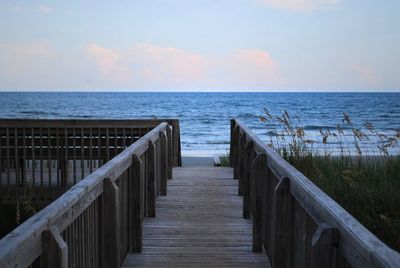 Wooden walkway leading towards sea against sky