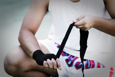 Midsection of boxer tying bandage while crouching on road