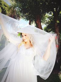 Smiling bride holding veil while standing on field