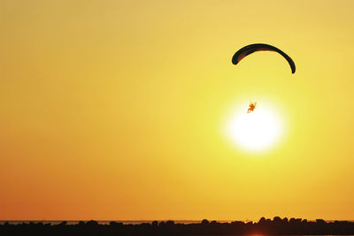 Person powered paragliding over sea against clear sky during sunset