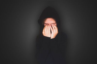 Person with eyes covered by hands against gray background