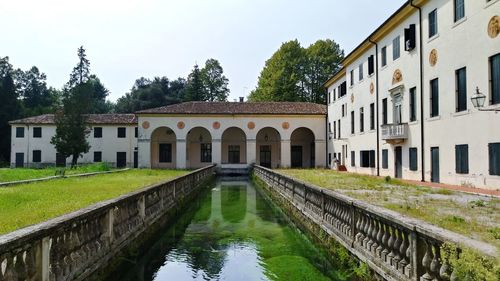 Arch bridge over canal amidst buildings against sky