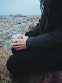 Midsection of woman sitting at beach against sky