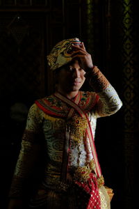 Woman looking away while standing against black background