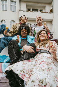 Happy multiracial friends eating ice cream against building