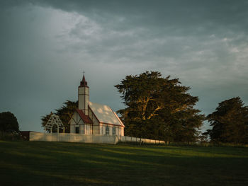 Low angle view of church by field against cloudy sky