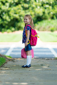 Side view portrait of schoolgirl with pink backpack standing on footpath