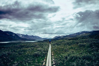 Footpath amidst field against cloudy sky