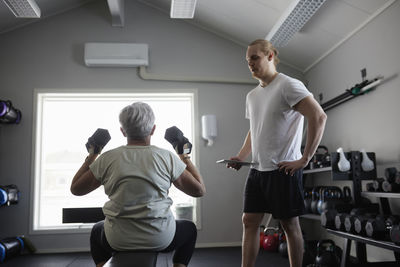 Woman exercising with dumbbell with trainer checking his progress