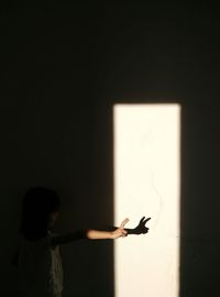 Rear view of girl showing peace sign against brightly lit wall