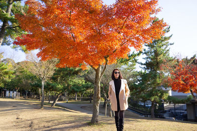 Portrait of young woman standing by tree during autumn