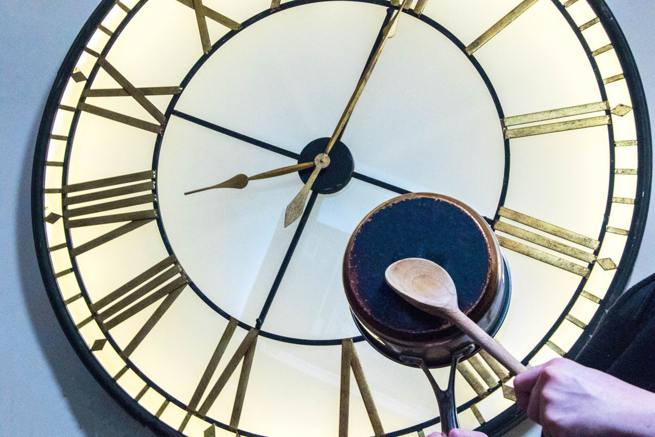 CLOSE-UP OF PERSON HOLDING CLOCK AGAINST WALL