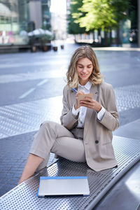 Portrait of young businesswoman using mobile phone while sitting in city