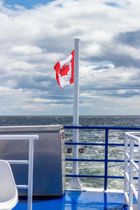 Red flag on railing by sea against sky