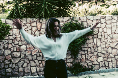 Full length of young woman standing against stone wall