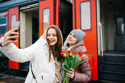 Girls with flowers on the station platform take a farewell selfie