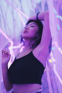 Young woman posing while standing against illuminated background