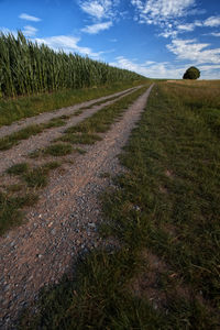 Dirt road on field against sky