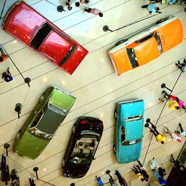 high angle view, multi colored, indoors, variation, in a row, transportation, land vehicle, large group of objects, mode of transport, day, built structure, no people, arrangement, incidental people, side by side, choice, hanging, car, sunlight