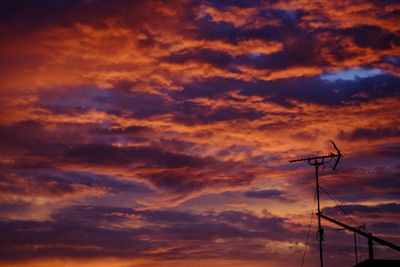 Low angle view of silhouette telephone pole against orange sky