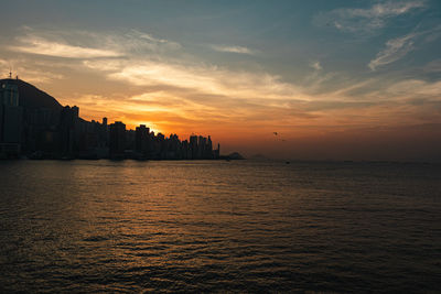 Silhouette buildings by sea against sky during sunset