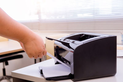 Cropped hands of businesswoman using computer printer on table in office