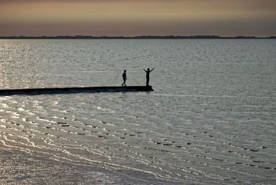 Silhouette person in sea against sky during sunset