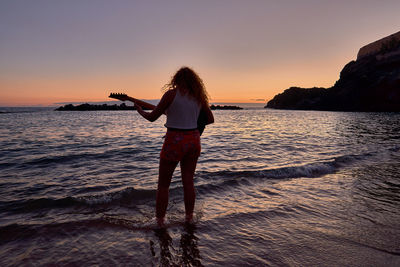 Woman standing at beach against sky during sunset
