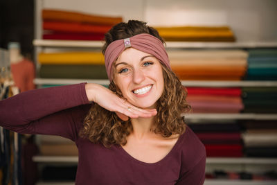 Cheerful fashion designer posing in her workshop surrounded by fabrics