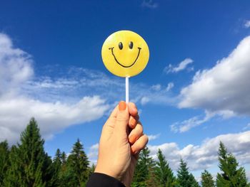 Close-up of hand holding smiley face candy against blue sky