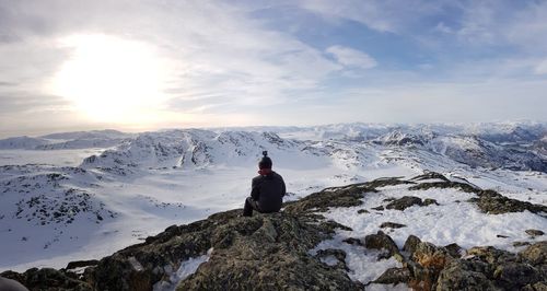 Rear view of person sitting on cliff during winter