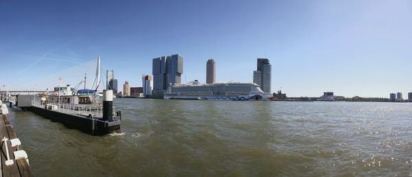 Cruise ship sailing in river by buildings against clear blue sky on sunny day