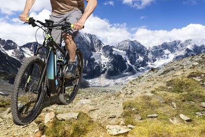 Low section of man on bicycle by mountains against sky