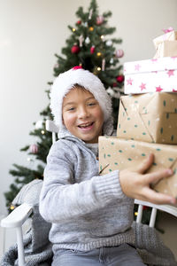 Portrait of happy boy holding gift box sitting against christmas tree