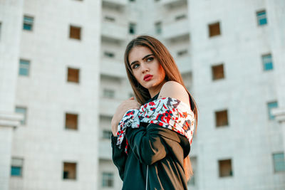 Portrait of a beautiful young woman standing against buildings