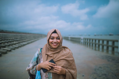 Portrait of smiling young woman standing against sky