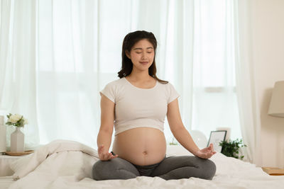 Pregnant woman meditating while sitting on bed