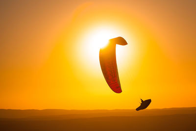 Silhouette bird flying against orange sky