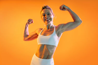 Portrait of young woman exercising against yellow background